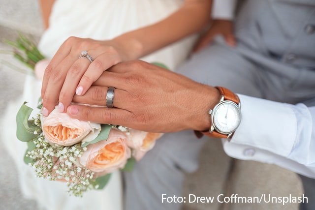 Ein Brautpaar hat gemeinsam seine Hände auf einen Blumenstrauß gelegt. 