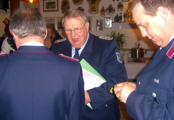 Der Vorsitzende des Landesfeuerwehrverbandes Lothar Lindecke zeichnet im Namen des Innenministers Lutz hanke für langjähriges, erfolgreiches Wirken in der Feuerwehr mit der silbernen Ehrenspange aus. Rechts: Gemeindewehrleiter Dirk Jeitner, der die Spange für das Anheften ans Revers vorbereitet.