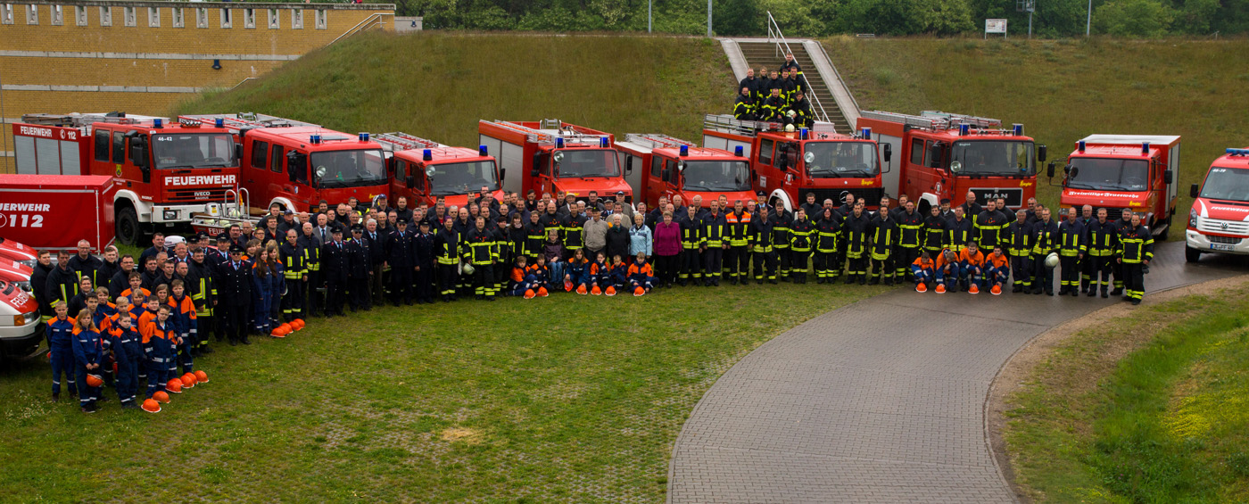 Gruppenfoto der Gemeindefeuerwehr von Möser, bestehend aus den Mitgliedern der sechs Ortfeuerwehren. Die Feuerwehrleute stehen in ihren Uniformen in Gruppen vor ihren Fahrzeugen.